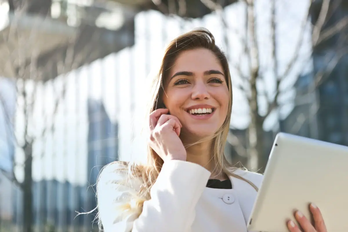 Confident businesswoman using her tablet and phone, smiling outdoors in sunlight.