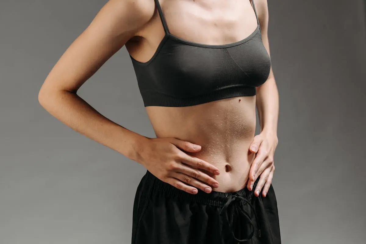 Close-up of a woman’s torso in a studio setting, emphasizing skin texture and athletic form.