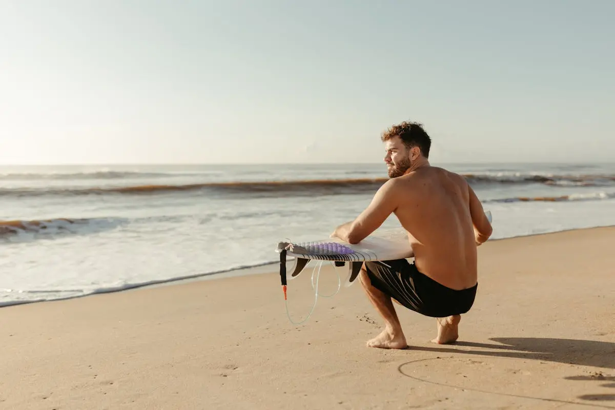 Man Crouching on the Beach with a Surfboard 