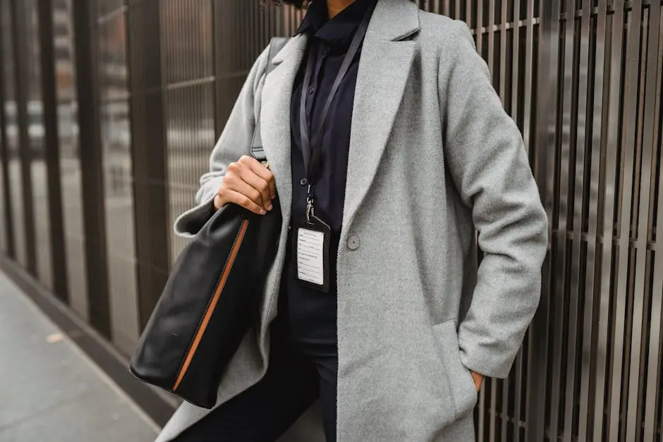 Crop anonymous female employee with badge standing with hand in pocket and shoulder bag on city pavement