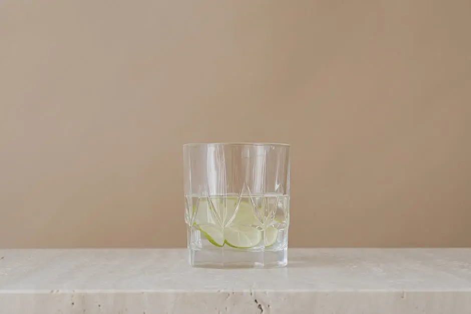 Minimalist image of lime-infused water in a clear glass on beige background.