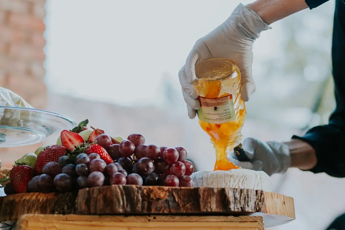 A person pouring honey on a wooden table with fruit
