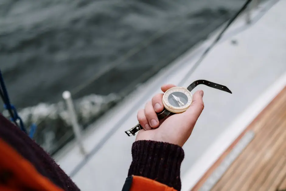 An adult holding an old-fashioned nautical compass on a sailboat at sea.