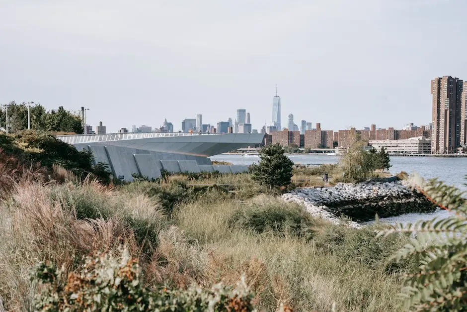 Tranquil Hudson River flowing between grassy embankment and modern city district with high rise skyscrapers and residential buildings placed in New York City in daytime