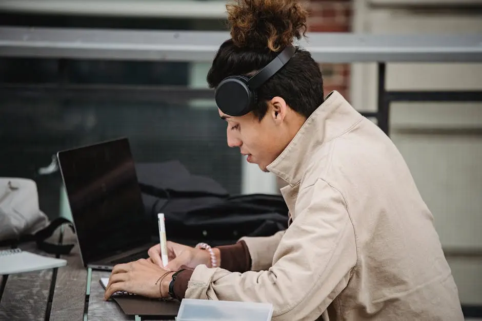 Young ethnic man in headphones taking notes neat laptop