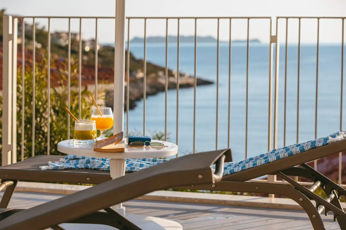 A serene oceanfront view from a terrace, featuring sun loungers and refreshing drinks on a sunny day.