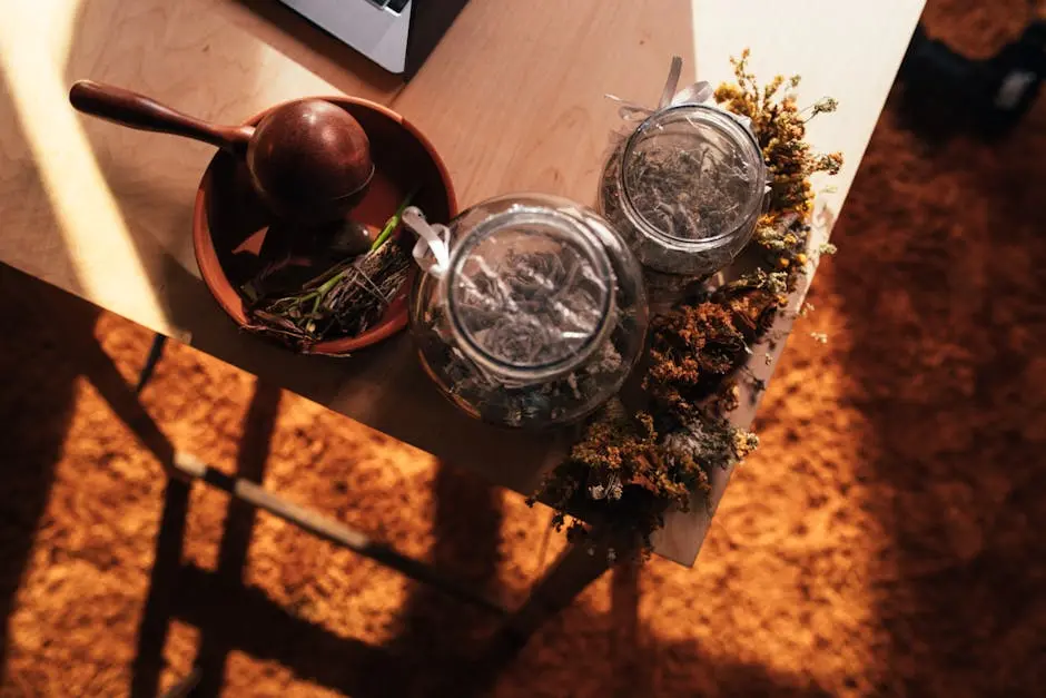 Top view of dried herbs, glass jars, and a mortar and pestle on a wooden table.