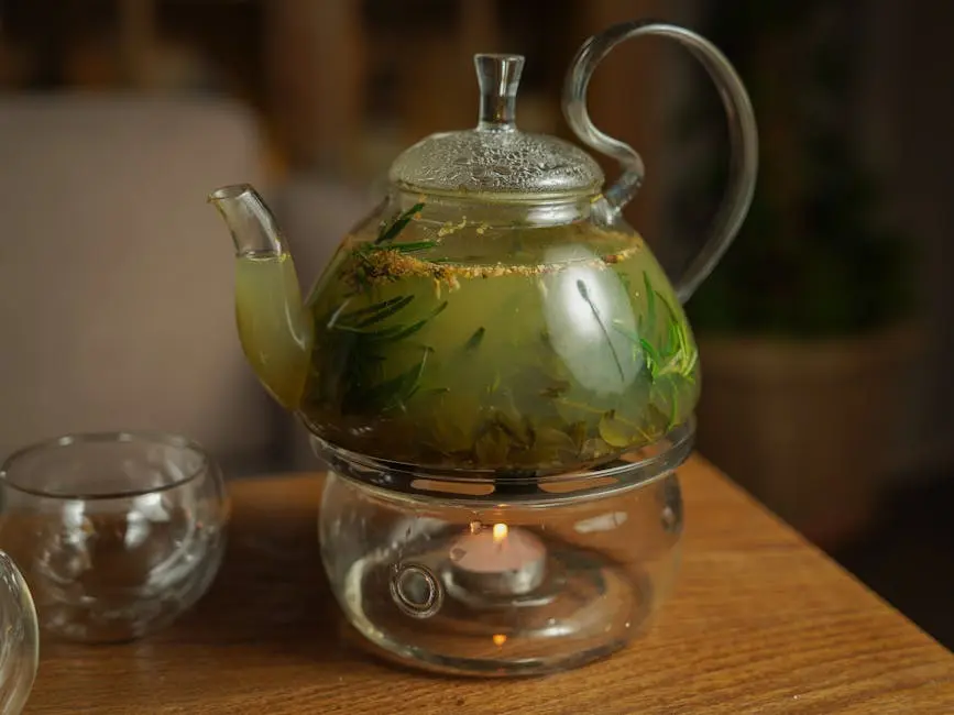 A clear glass teapot with herbal infusion warming over a candle flame on a wooden table.