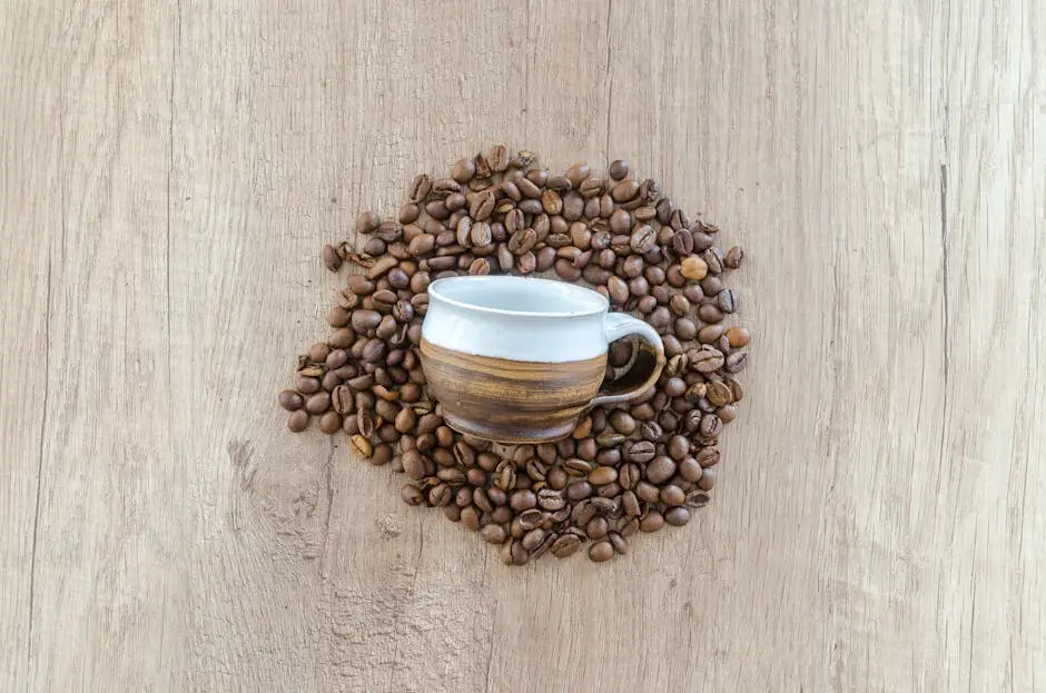 A rustic ceramic cup surrounded by coffee beans on a wooden surface, top view.