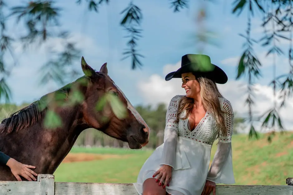 A joyful cowgirl interacts with a horse outdoors under a bright sky.