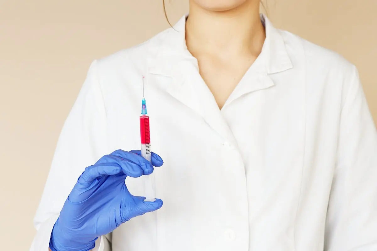 Crop unrecognizable female nurse in medical uniform and latex gloves with syringe in hand ready to give a vaccine