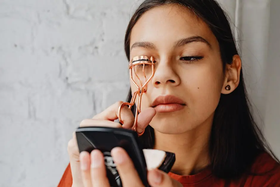 Close-up portrait of a young woman curling her eyelashes with focus on beauty and self-care.