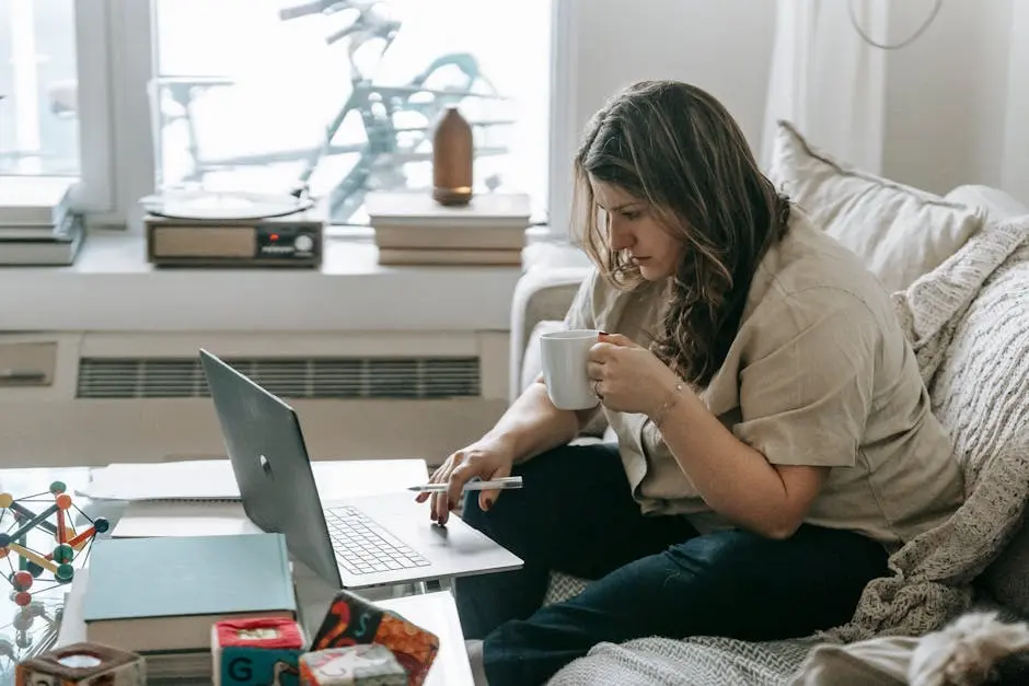 Vrouw met kopje op bank terwijl ze aan laptop werkt