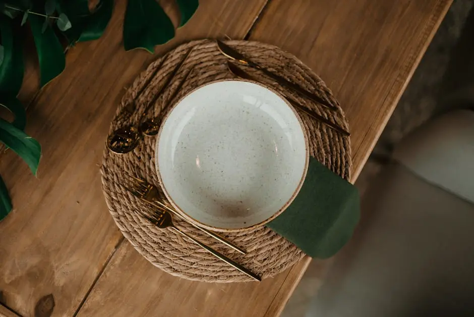 A top view of a rustic dining setup featuring a ceramic bowl and gold cutlery on a woven placemat.