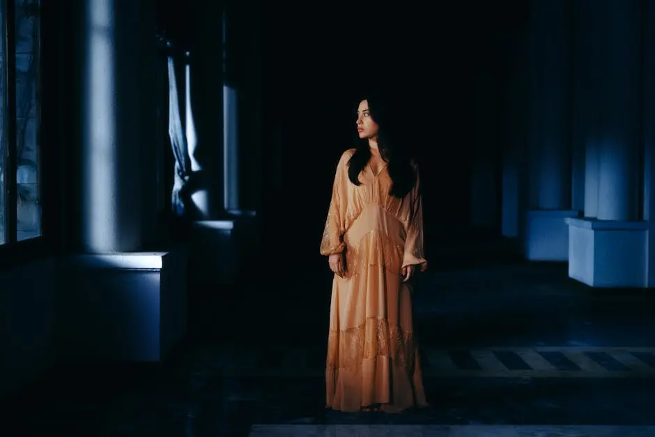 A woman in a flowing dress stands in a dimly lit hallway, exuding elegance and mystery.