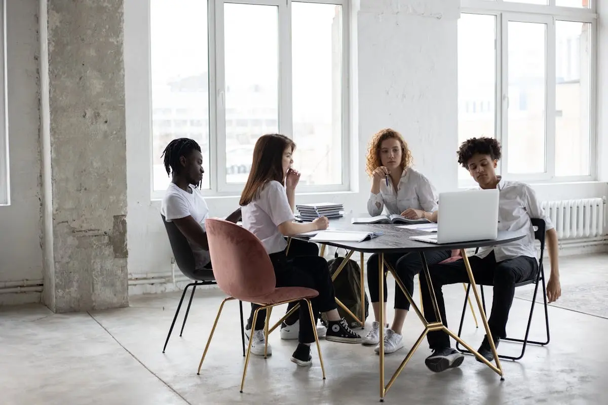 Full length concentrated multiethnic coworkers in formal wear working on project together and gathering at desk in light loft workplace