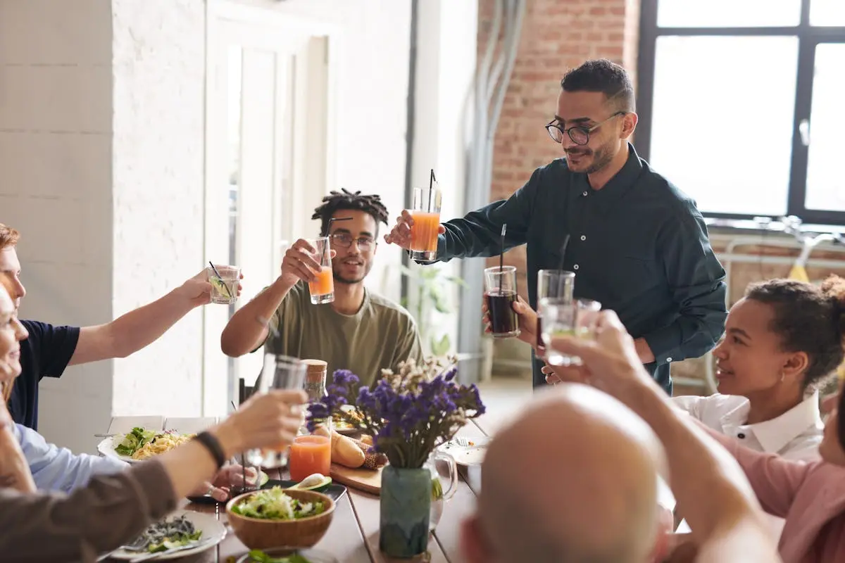 Group of friends toasting drinks during a lively indoor meal, enjoying togetherness and celebration.