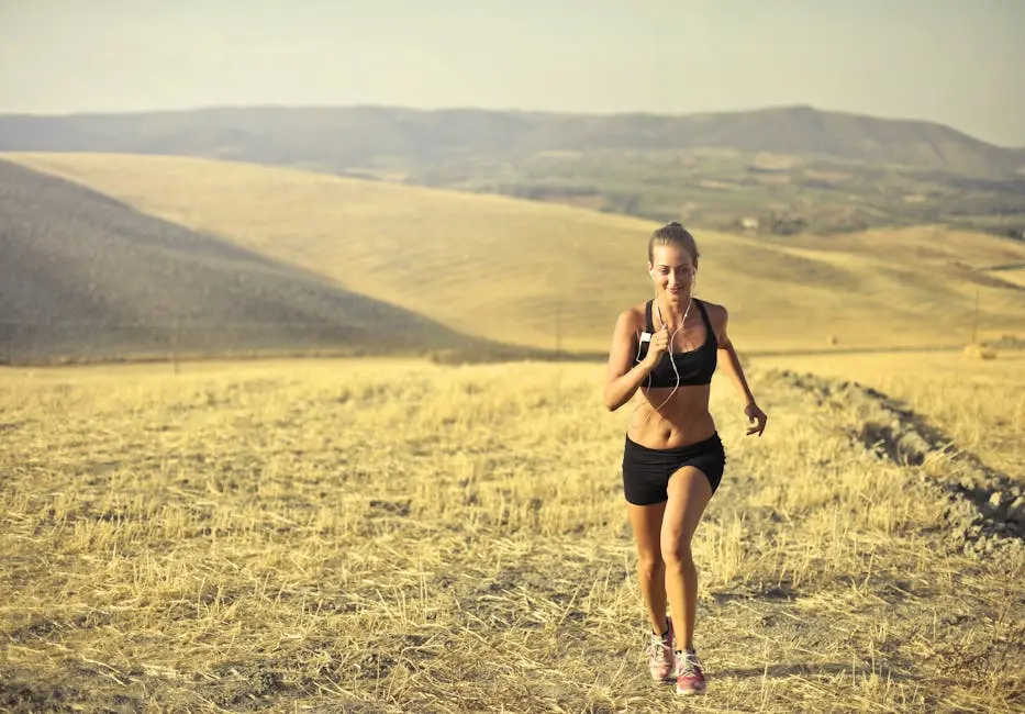 Powerful young female athlete in activewear running along hill on background of mountainous landscape and listening to music in earphones during cardio training