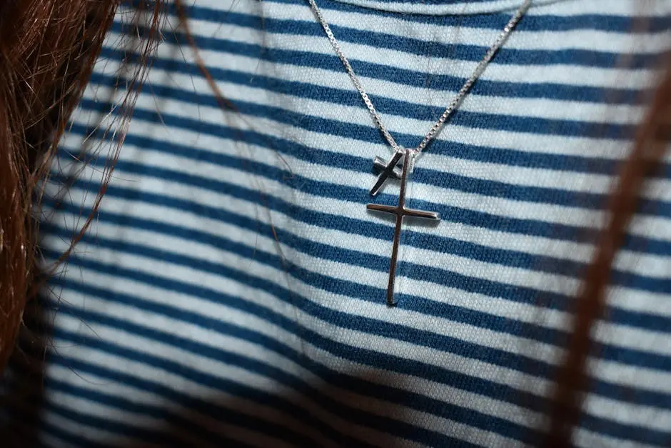 A silver cross necklace showcased on a blue and white striped shirt, highlighting minimalist fashion.