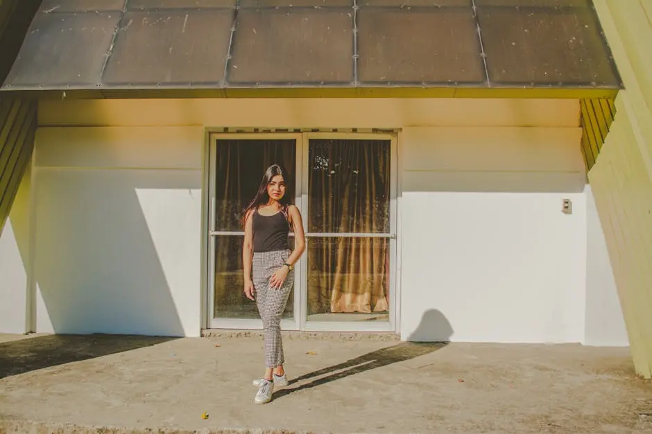 A woman standing in front of a modern house with large glass doors in daylight.