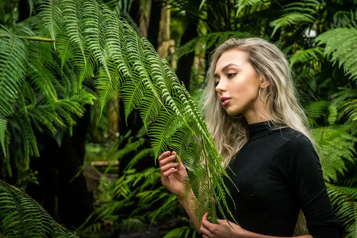 A striking portrait of a blonde woman amidst vibrant green ferns, capturing natural beauty.