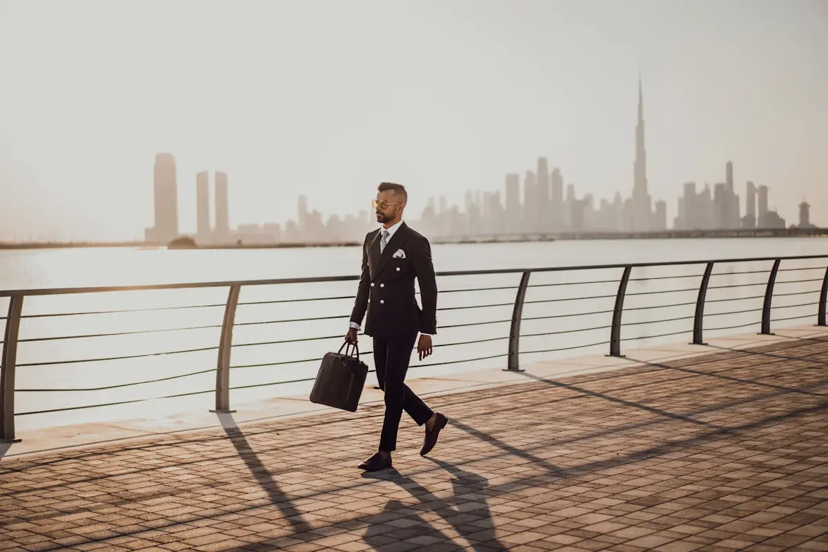 Man Walking on Pavement While Holding a Bag