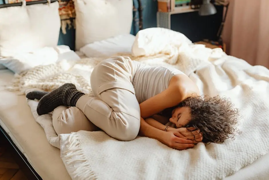 A young woman sleeps peacefully in a fetal position on a bed, surrounded by soft pillows and warm blankets.