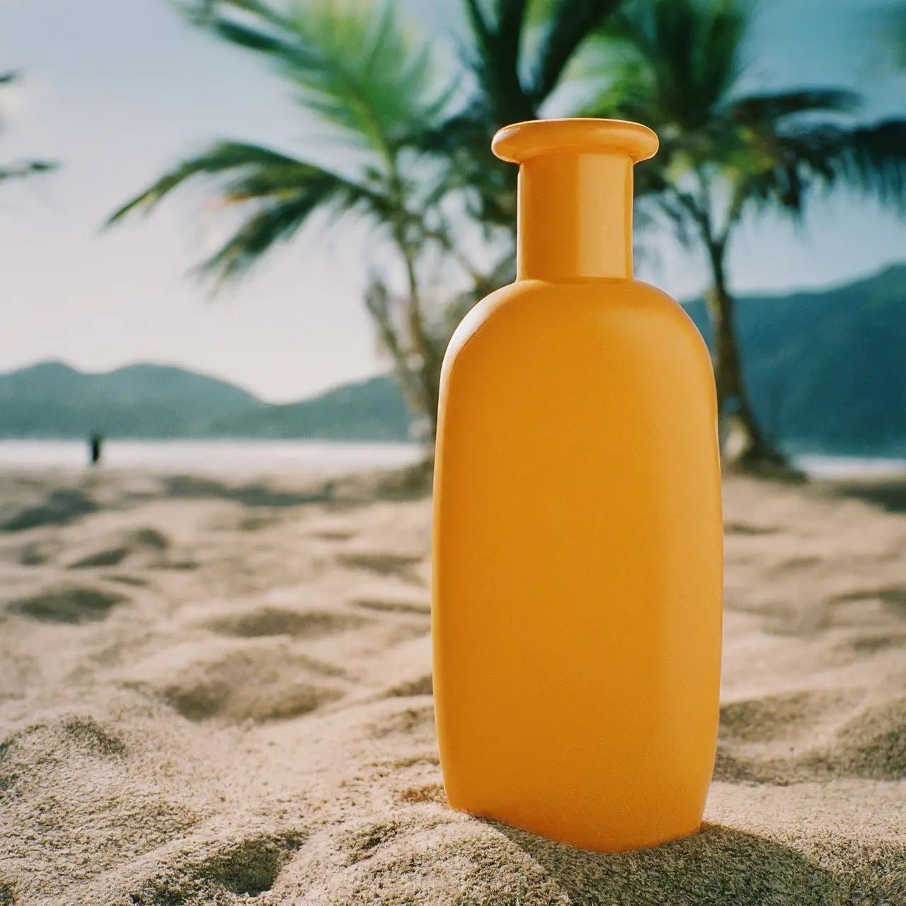 Sunscreen bottle on a sunny beach with palm trees. 35mm stock photo