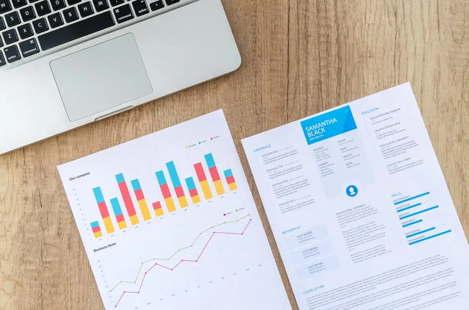 Top view of a laptop, charts, and resume on a wooden desk, showcasing business analysis and job application.