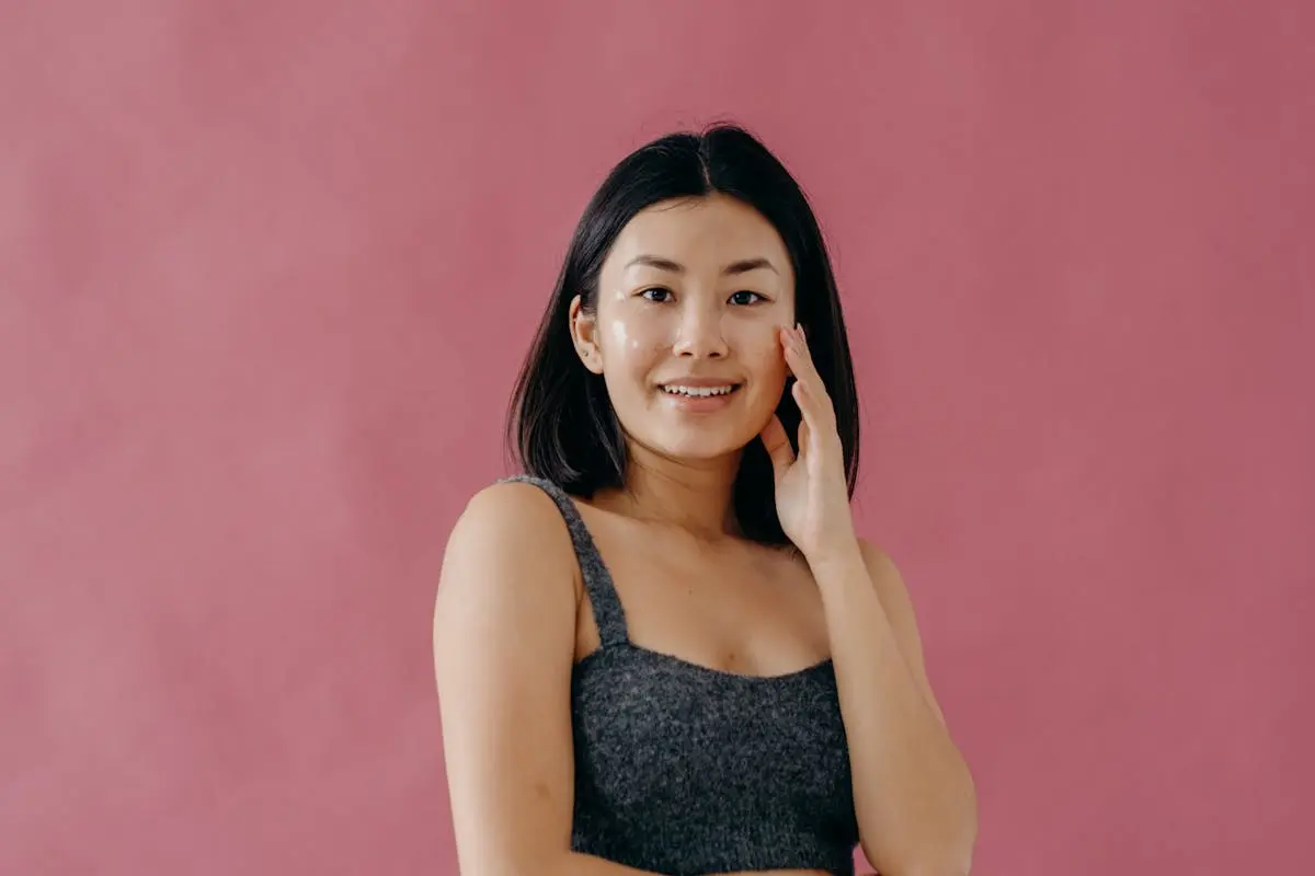 A Woman in Gray Tank Top Smiling while Touching Her Face