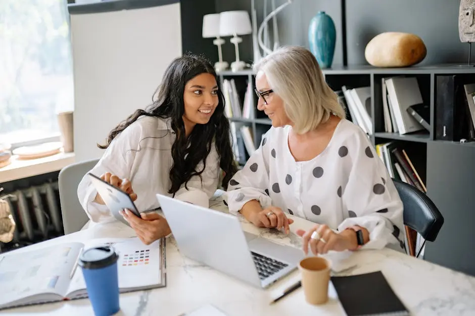 Two businesswomen engaged in a productive meeting around a laptop and tablet in a contemporary office.