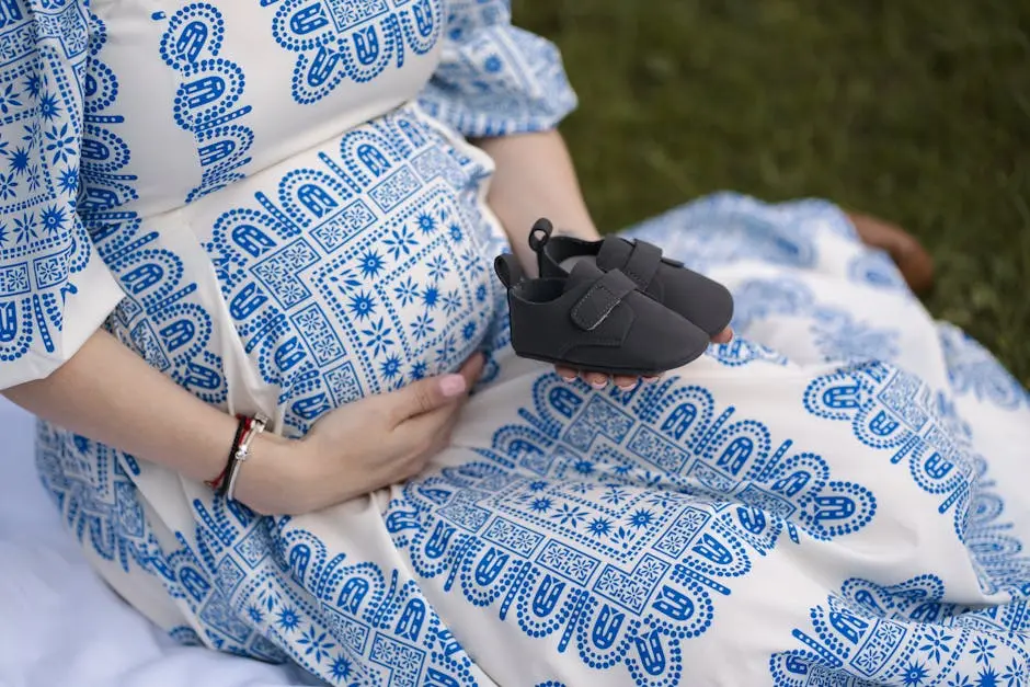 A pregnant woman gently cradles her baby bump while holding a pair of small black baby shoes in one hand. She is wearing a blue and white patterned dress, symbolizing the connection between pregnancy, Semaglutide, and the careful considerations around using medications like Semaglutide (Ozempic, Wegovy) during pregnancy. Highlighting the essence of pregnancy, fertility, weight management, type 2 diabetes treatment, and the importance of consulting healthcare providers about the potential risks and benefits of Semaglutide for pregnant patients.