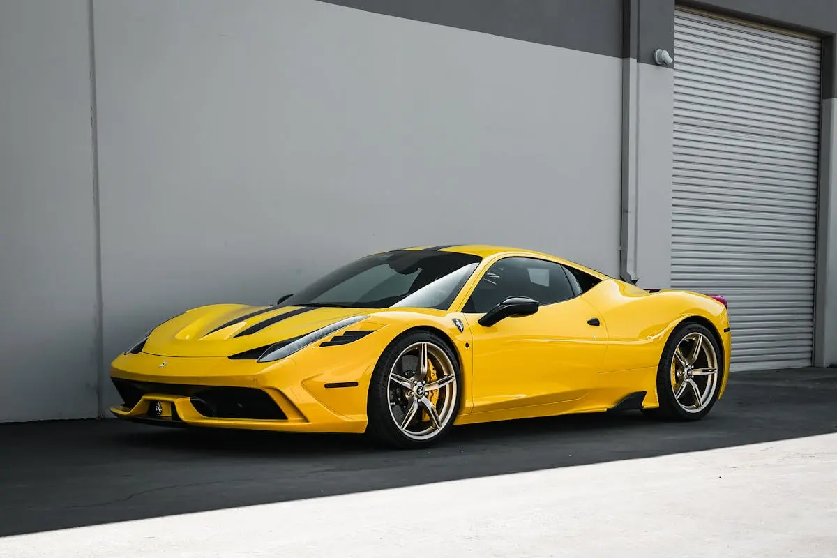 A sleek yellow sports car parked beside a modern building with industrial surroundings.