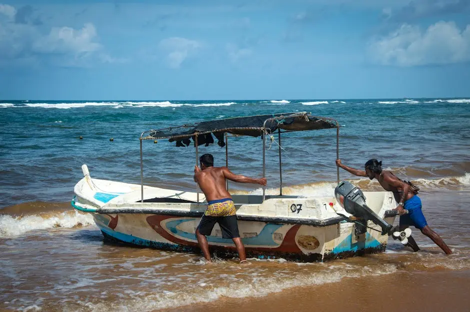 Two men pushing a small motorboat into the sea on a sandy beach under a clear blue sky.