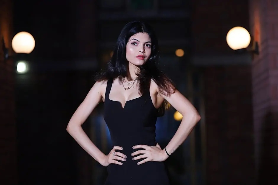 Stylish woman in a black dress posing confidently outdoors at night.