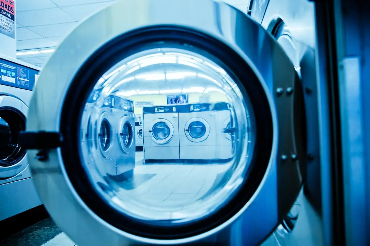 Interior view of a modern laundromat with rows of steel washing machines.