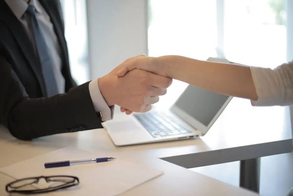 Close-up of a professional handshake over a laptop during a business meeting in an office.