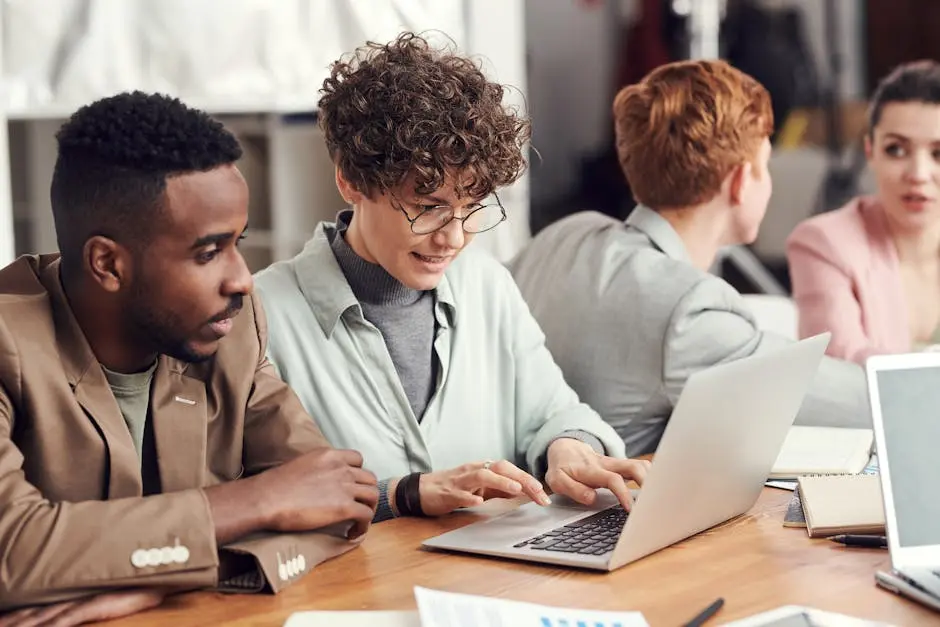 A group of diverse professionals engaged in a team meeting, working on laptops in a modern office setting.