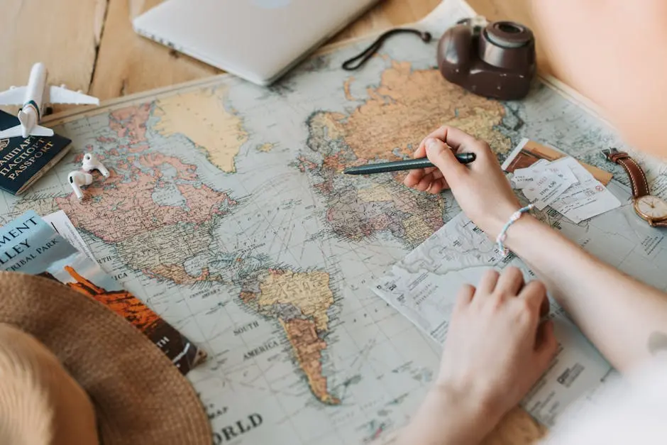 Hands marking destinations on a world map surrounded by travel essentials like passport and camera.