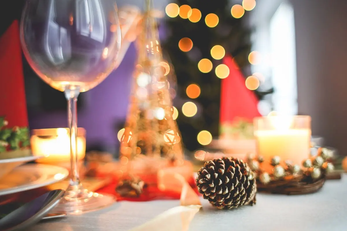 A warm and inviting Christmas table setting with candles, pinecones, and a wine glass.