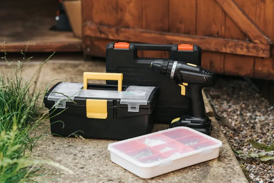 A collection of toolboxes and a power drill on a concrete surface near a garage.