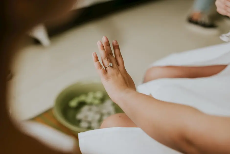 A close-up of a woman’s hand adorned with a diamond engagement ring, captured indoors.