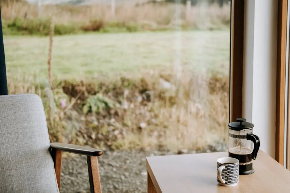 French press with aromatic espresso near ornamental mug on table against glass wall in countryside house