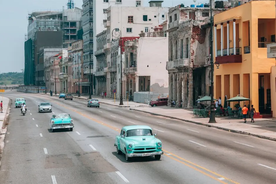 Classic vintage cars drive along a bustling street in Havana, showcasing vibrant architecture and retro charm.