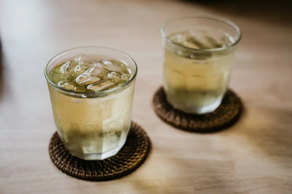 Two glasses of iced tea with ice cubes sit on coasters on a wooden table.