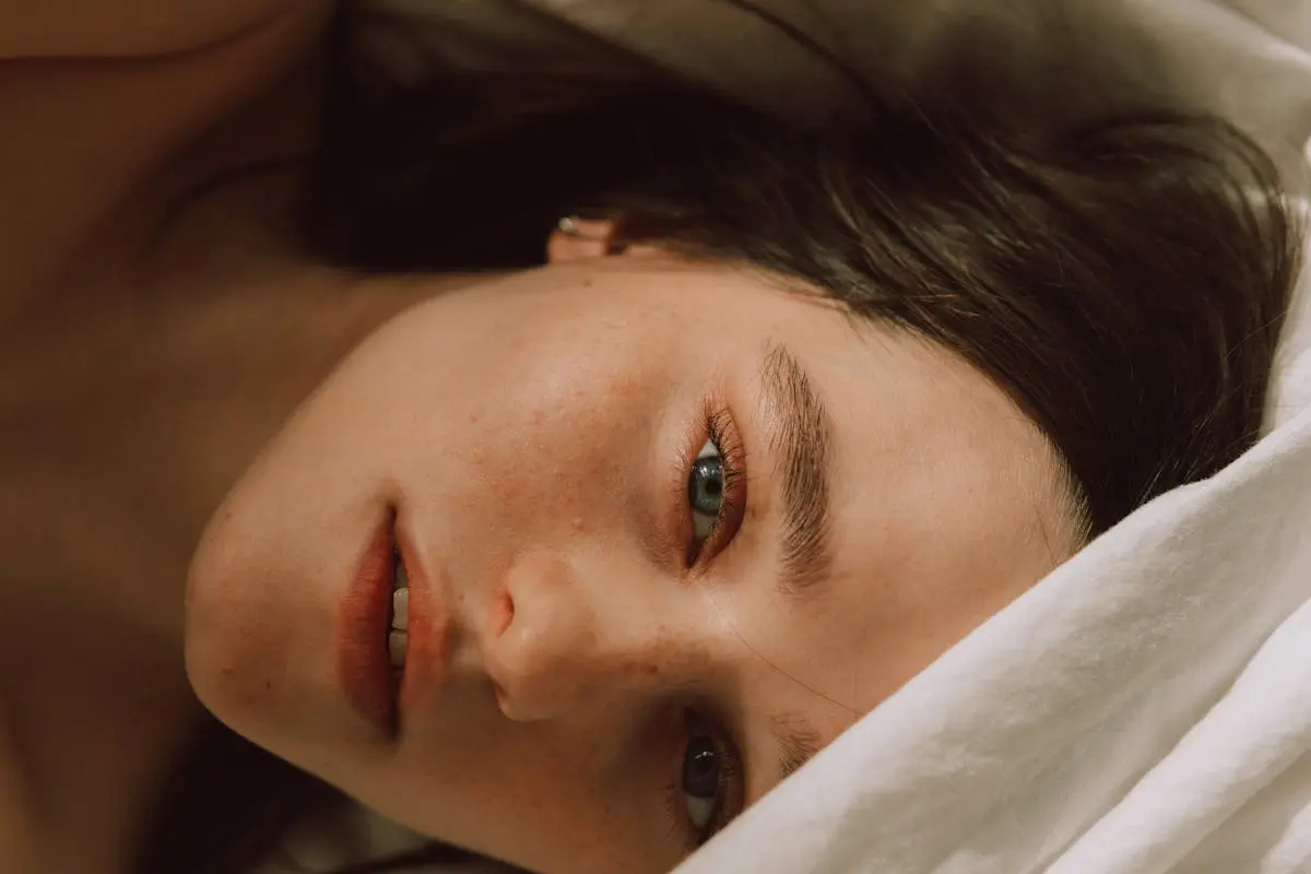 Captivating portrait of a young woman with freckles lying on a bed, enveloped in soft light.