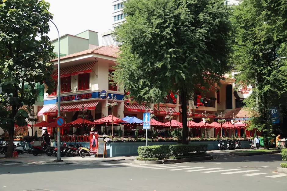 Lively urban cafe with red awnings in a vibrant city setting, surrounded by lush greenery.