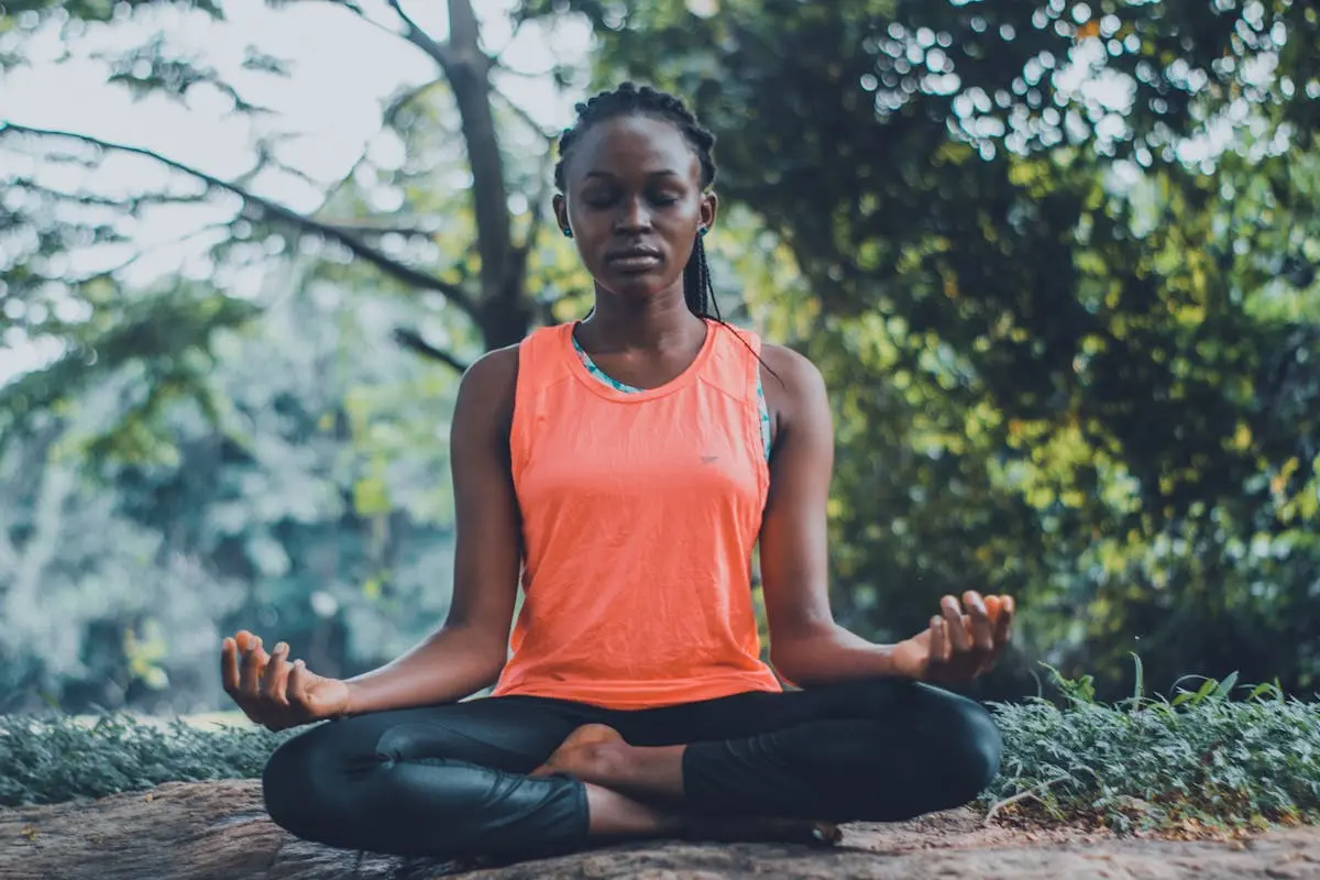 A woman meditating peacefully outdoors in a lush green setting, promoting relaxation and mindfulness.