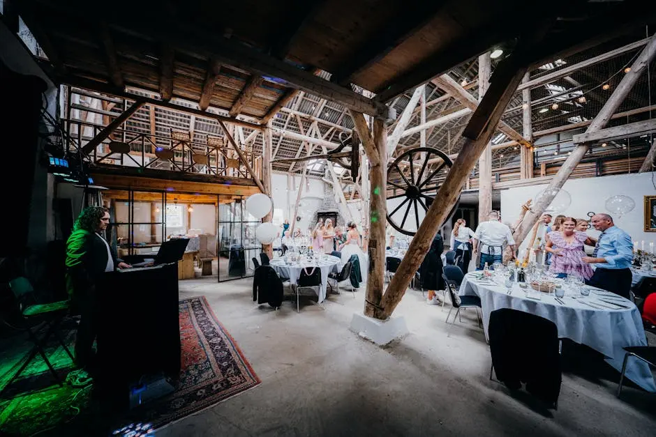 A vibrant wedding reception in a rustic barn setting with guests and a DJ.