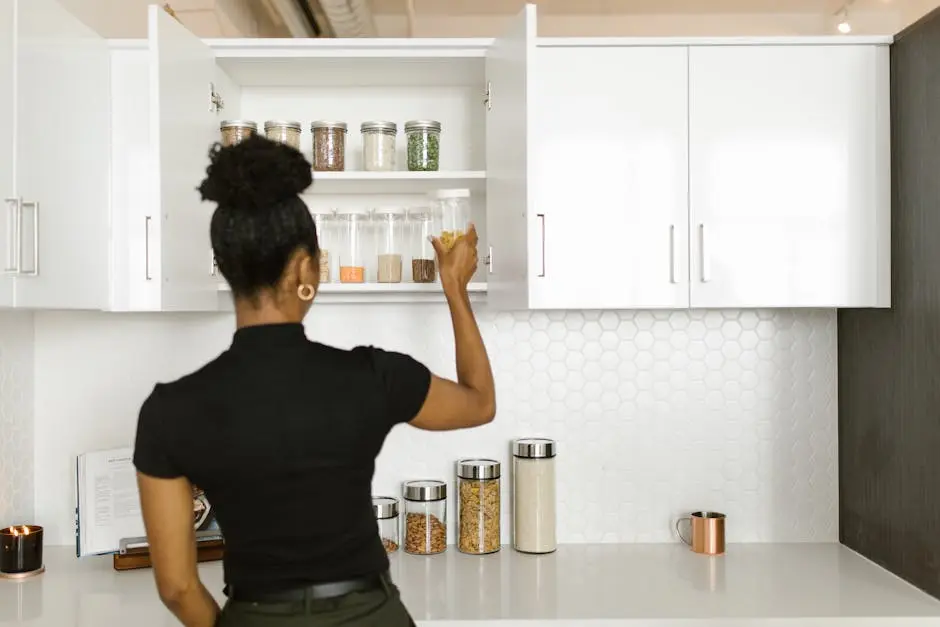 A woman organizing a pantry shelf with various food jars in a modern kitchen.